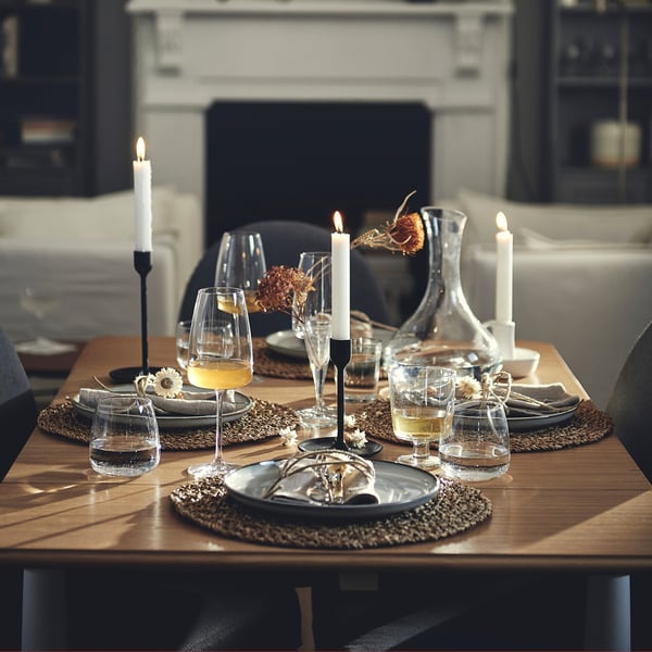Wooden dining table with 4 place settings, candles, and glasses. Comfortably seats two. Larger than nearby chairs.