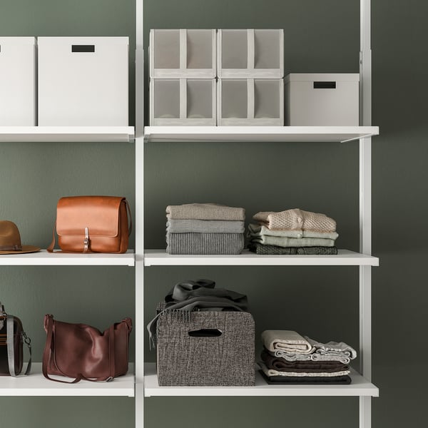 Shelf storage system with boxes, folded clothes, and handbags against a green wall.