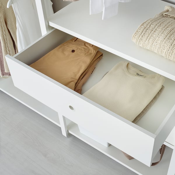 Open white drawer unit showing neatly folded beige pants and cream sweater, part of adjustable storage system.