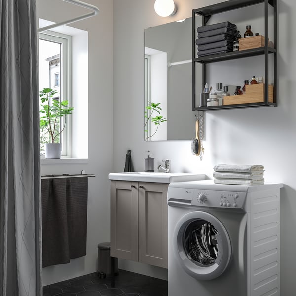 Modern grey bathroom with white appliances, mirror cabinet, vanity, washing machine, plant, and folded towels.
