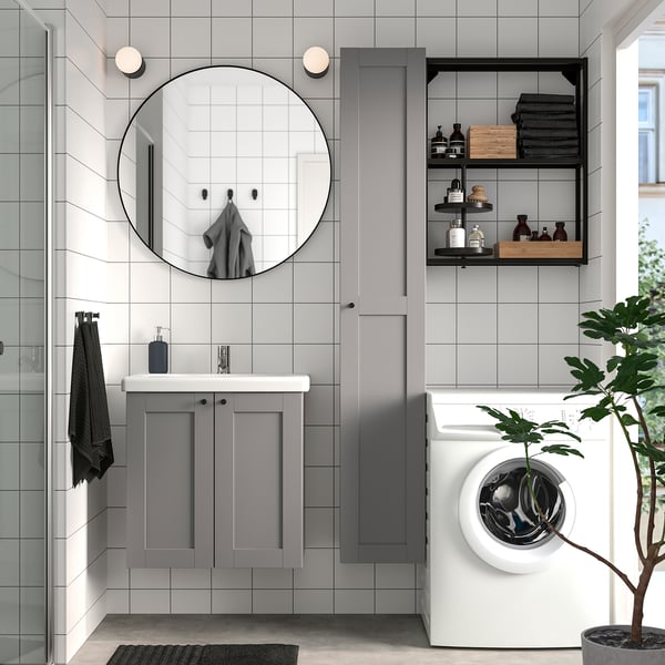 Modern bathroom with grey ENHET cabinets, large round mirror, white washing machine, potted plant, and black accents.