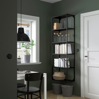 Modern home office with ENHET black shelf, holding books and vases. Beside a white desk with chair, plant, and white door.
