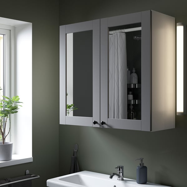 ENHET mirror cabinet in grey above sink, illuminated, with soap dispenser.
