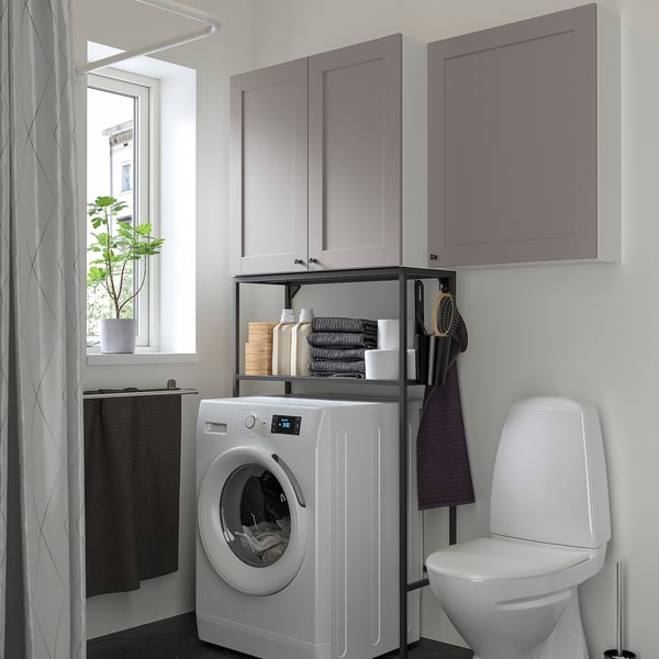 Modern, compact bathroom with ENHET grey storage. Washing machine and toilet; shelves hold items.