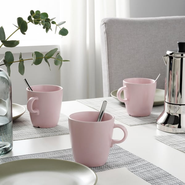 Three pink mugs and a coffee maker on table with place mats; decorative plants.