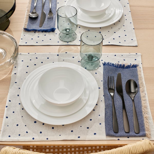 Table set with white plates, bowls, glasses, and cutlery on blue-spotted placemats.