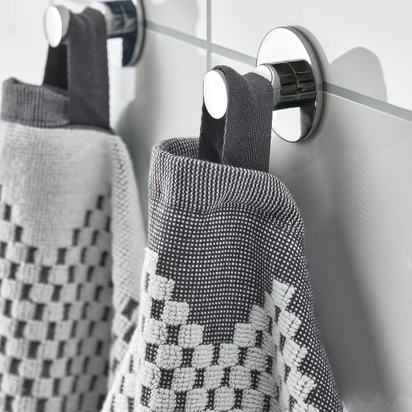 Two patterned towels hang on chrome hooks on a shower screen.