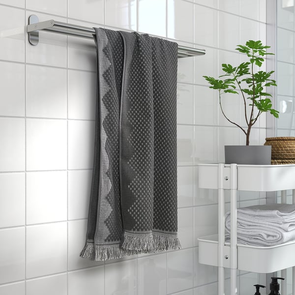 Modern bathroom with FJÄLLSTARR dark grey towel on rack, white tiles, and small plant on corner shelf.