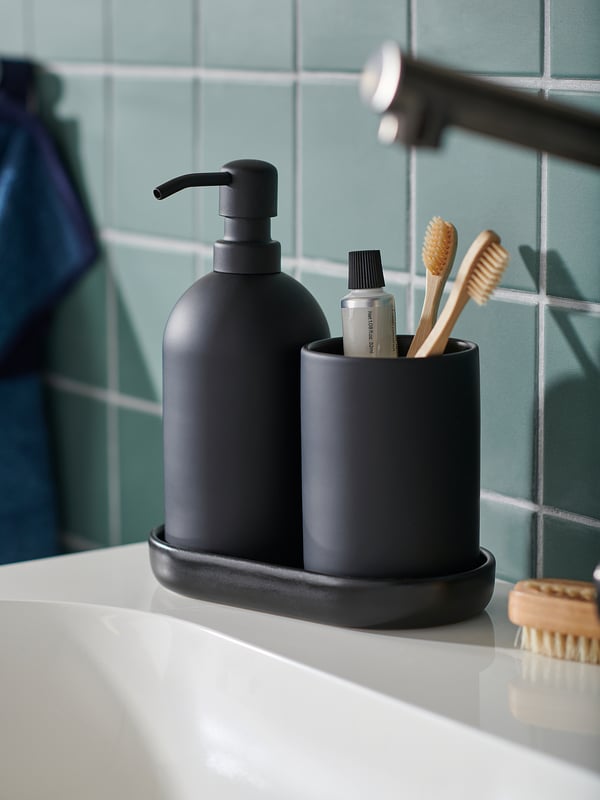 Grey soap dispenser & toothbrush holder on white counter with rustic brushes.