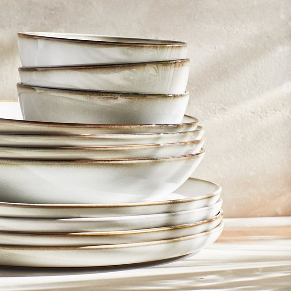 Stacked GLADELIG ceramic dishes in sandy glaze on table.
