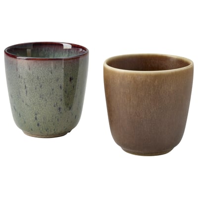 Two ceramic cups, one green with dark spots, one brown, rustic, handcrafted design, rested on a white surface.