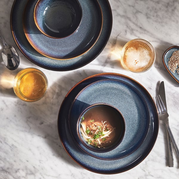 Top view of a meal set with GLADELIG blue stoneware plates, bowls, and cutlery on a marble surface.
