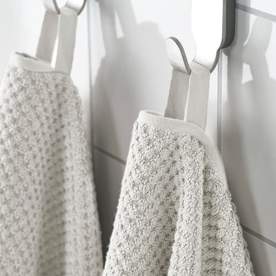 Two beige towels hang side by side on hooks, displaying their soft, fluffy texture and medium thickness, perfect for absorbing and daily use.