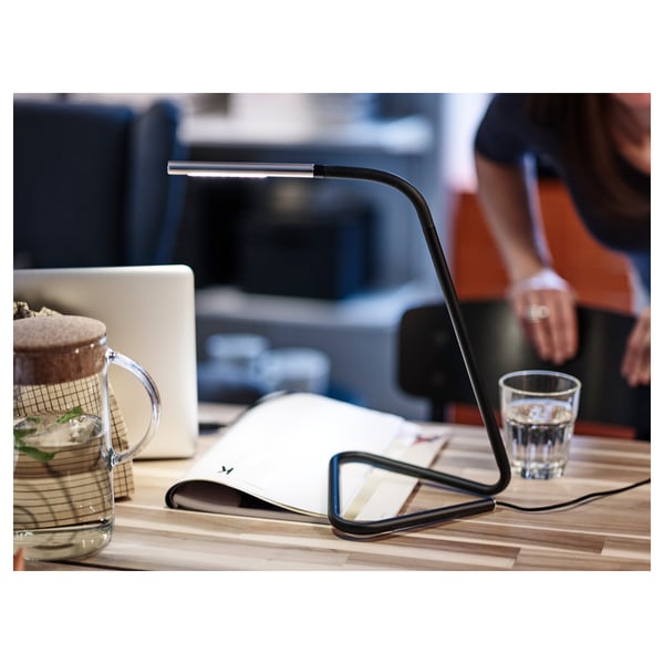 A sleek, adjustable desk lamp with warm white led light shines down on a book and glass.