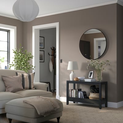 Modern living room with HAVSTA console table, round mirror, plants, lamp, and grey sofa with striped pillows and beige throw.