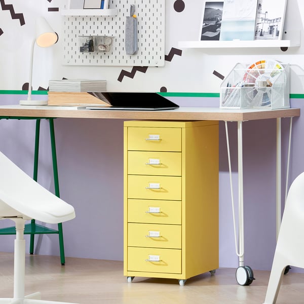 Bright yellow HELMER drawer unit, made of steel, with five drawers. Small, fits under wooden desk, near white chair. Castors for mobility.