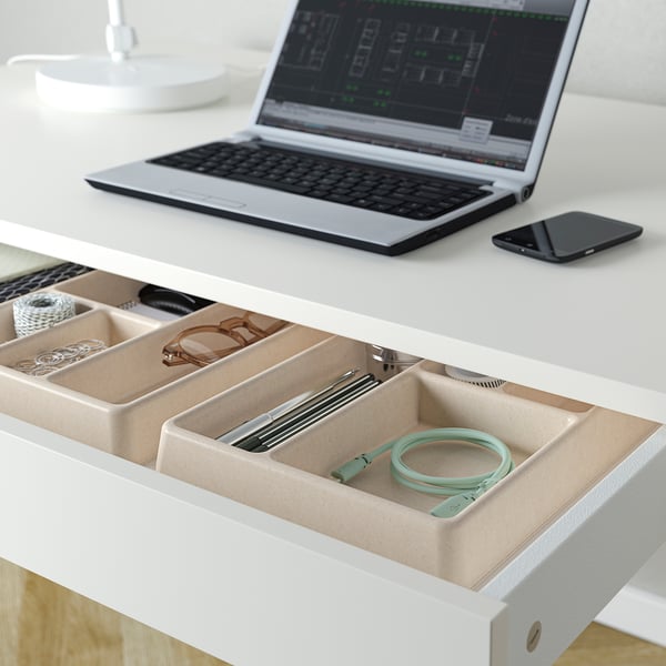 Open laptop on desk, with open storage tray holding green cable, pens, and small items.