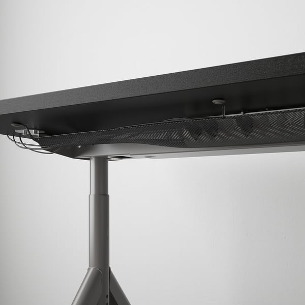 Black desk with adjustable legs and cable management net beneath the tabletop.