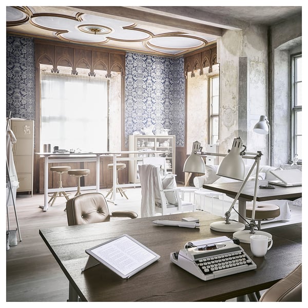 Vintage-style office with wooden desks, chairs, and typewriters. Blue patterned wallpaper and ornate ceiling. Bright, cosy atmosphere.