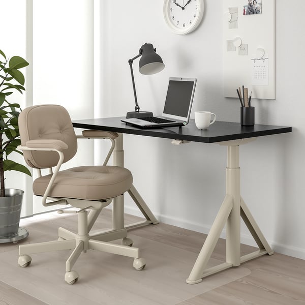 Black desk, ergonomic chair with wheels. Minimalist workspace with plant.