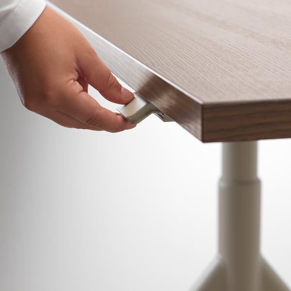 Hand adjusts metal lever under wooden desk edge, demonstrating height adjustment feature.