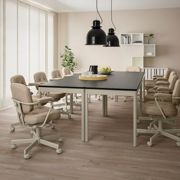 Modern conference room with IDÅSEN table, chairs, lights. Table set with tray, cups, fruit. Wood floors, books, plants.