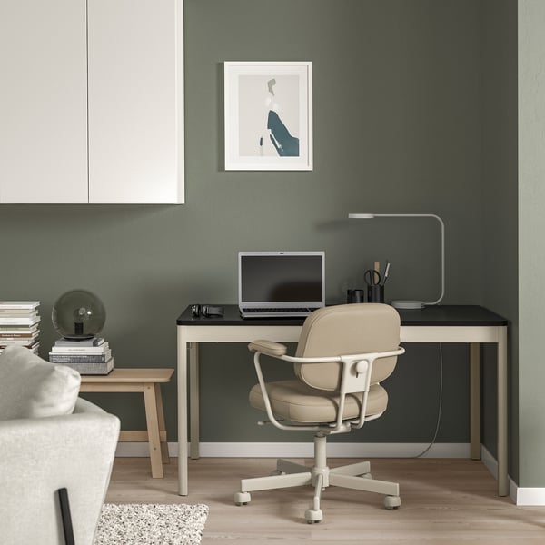 Minimalist home office with green wall, black desk, laptop, lamp, chair, globe, books, and artwork.