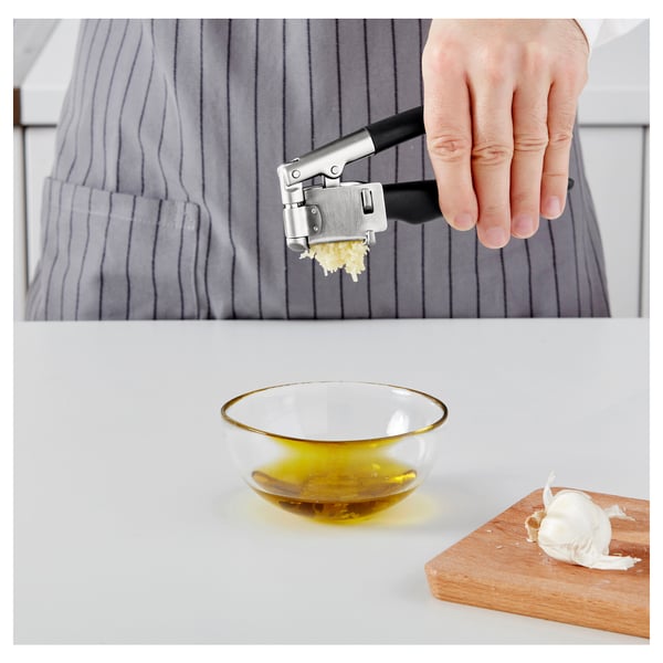 Person uses garlic press over bowl of oil. Garlic cloves are minced into bowl.