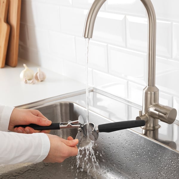 Person presses garlic under running water from a stainless steel tap in a kitchen sink.