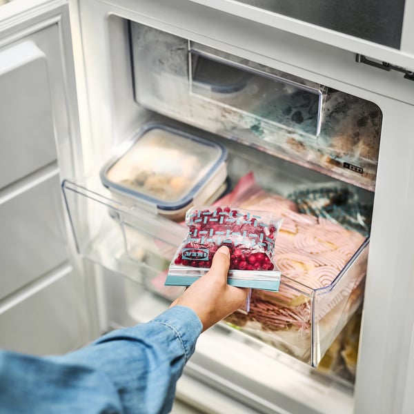 Person holding reusable, transparent food bag labelled ISTAD with red contents from freezer drawer.