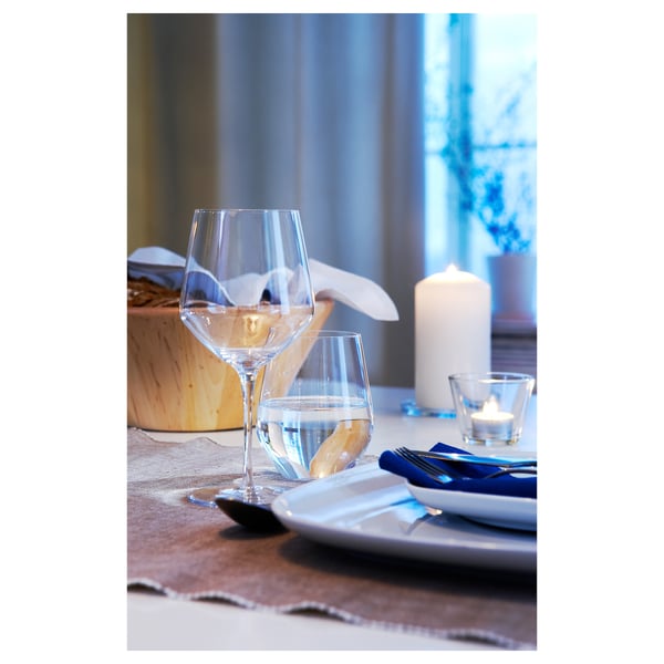 Clear wine glass on table with candle, napkin, and plate. Simple elegant design.