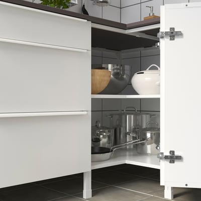 Open white corner cabinet shows organised pots, pans, lids, wooden bowl, and teapot. Soft-closing hinges visible.