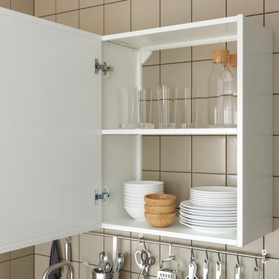 Open white cabinet displays neatly stacked bowls, plates, glasses, and bottles. Soft close hinges visible.