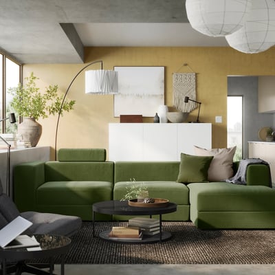 Modern living room with olive sofa, plant, lamps, art, rug, concrete.