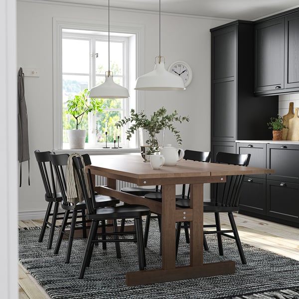 Modern kitchen with black KLIMPFJÄLL table & chairs, wooden floor, black cabinets, white pendant lights, green plants, and a white clock.