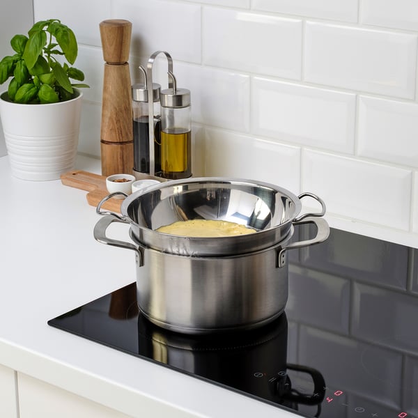 Stainless steel double boiler insert sits on stove, containing creamy mixture. Perfect for gentle cooking of sauces or melting chocolate.
