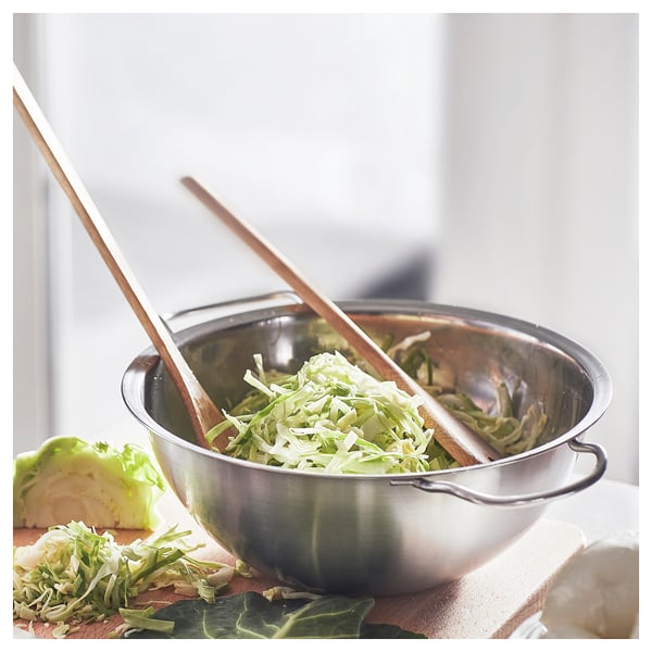 Silver double boiler sits on a counter, filled with shredded cabbage. Wooden tongs rest inside, ready for serving.