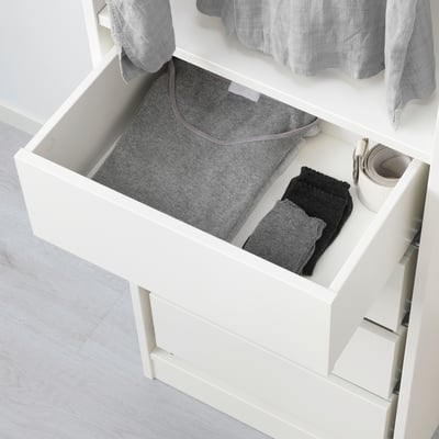 An open white drawer from the KOMPLEMENT series, with folded clothes and a box inside, designed for organising small items.