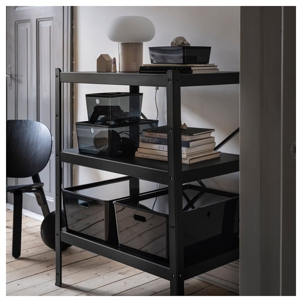 Black 3-tier shelving with books, tech, lamp, wall, door, chair.