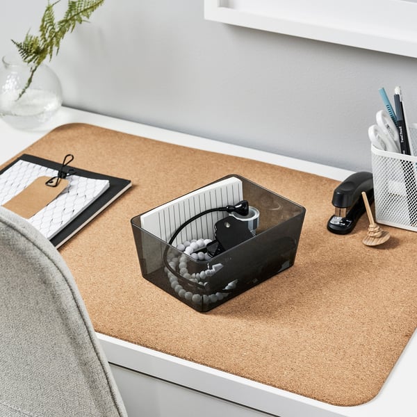 KUGGIS black storage box on desk mat holding cables, surrounded by office supplies and a plant.