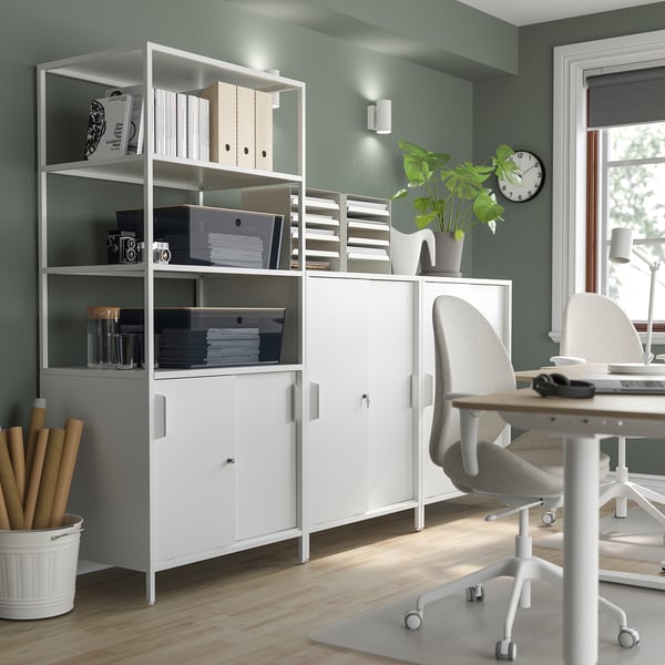 Well-organized home office with white KUGGIS storage units, grey chairs, wooden table, green plant, and wall clock.