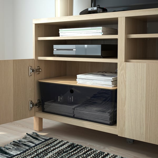 Wooden cabinet with open door revealing stacked books and plastic storage boxes.