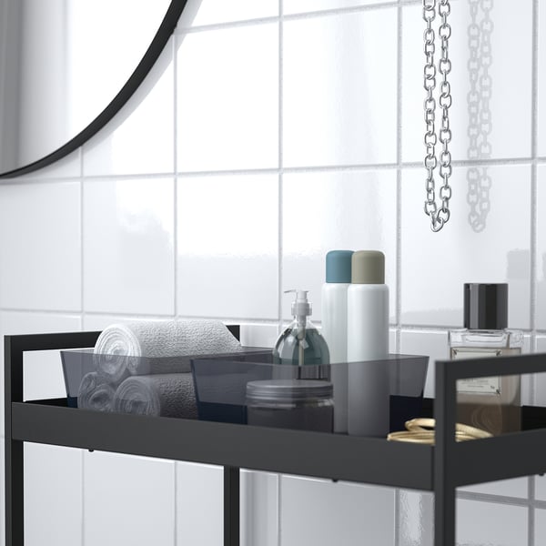 Black metal shelf in bathroom holding towels, toiletries, and a small box, ideal for organising.