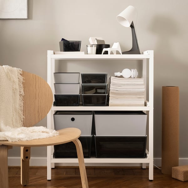 Modern white office: chair with blanket, storage unit, lamp, books, and blanket.