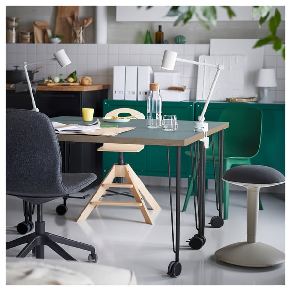 Modern home office setup with a blue LAGKAPTEN desk, grey chair, green stools, and adjustable lamps.