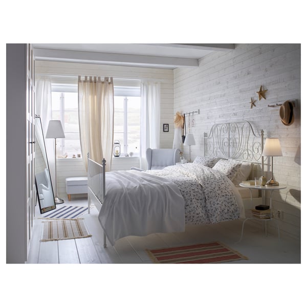 Bright, white, steel-framed bed with curved head and footboards, set against a window with sheer curtains, featuring a cosy, inviting bedroom scene.