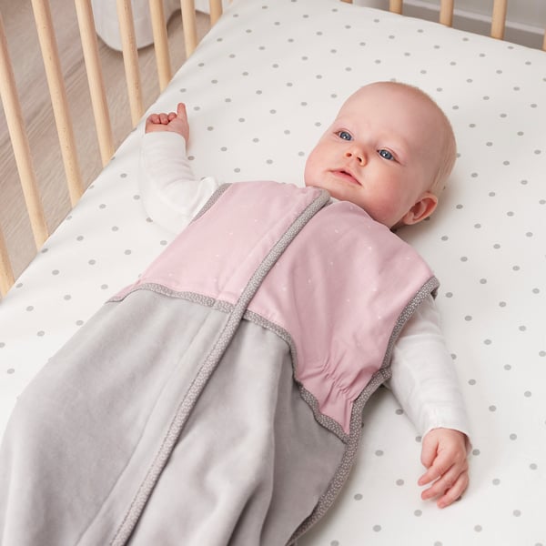 Baby in pink sleep bag on white polka dot cot sheet.