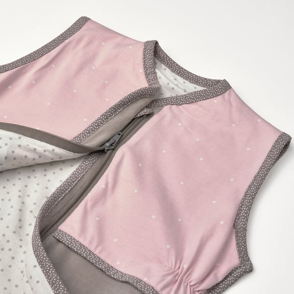 Light pink baby sleep bag with grey polka dot pattern and trim, showing soft fabric and secure zip.