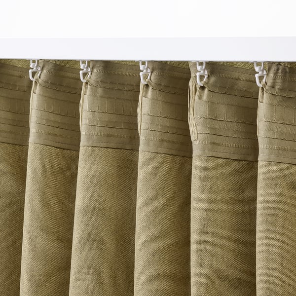 Green block-out curtains with hooks, partially closed, showing their pleated texture and light-following ability.