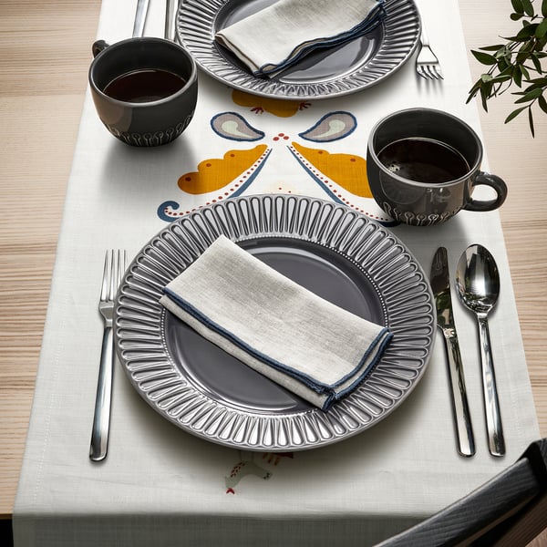 Table setting with grey plates, cups, silverware, white napkins, and embroidered table runner with hearts and horses.